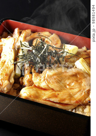 タレがたっぷりかかった熱々の炭火焼き鳥重を黒背景で撮影 98981494