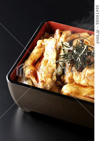 タレがたっぷりかかった熱々の炭火焼き鳥重を黒背景で撮影 98981495