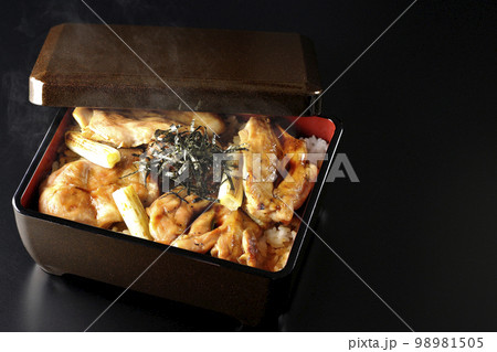 タレがたっぷりかかった熱々の炭火焼き鳥重を黒背景で撮影 98981505