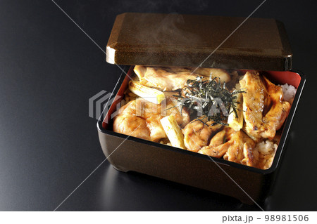 タレがたっぷりかかった熱々の炭火焼き鳥重を黒背景で撮影 98981506