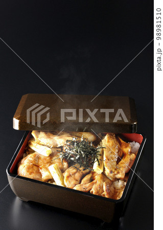 タレがたっぷりかかった熱々の炭火焼き鳥重を黒背景で撮影 98981510