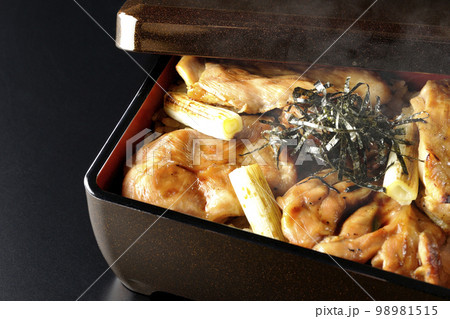 タレがたっぷりかかった熱々の炭火焼き鳥重を黒背景で撮影 98981515