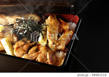 タレがたっぷりかかった熱々の炭火焼き鳥重を黒背景で撮影 98981518