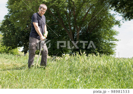 A man with an electric lawn mower mows the grass. For a gardening equipment store with a place for text. 98981533