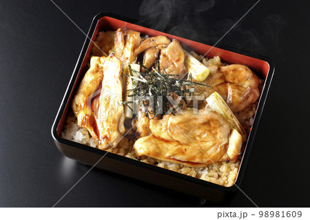 タレがたっぷりかかった熱々の炭火焼き鳥重を黒背景で俯瞰撮影 98981609