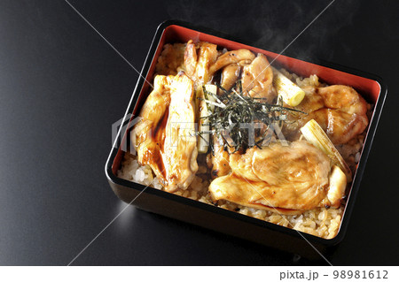 タレがたっぷりかかった熱々の炭火焼き鳥重を黒背景で俯瞰撮影 98981612