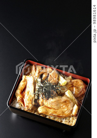 タレがたっぷりかかった熱々の炭火焼き鳥重を黒背景で俯瞰撮影 98981614