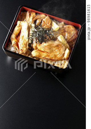 タレがたっぷりかかった熱々の炭火焼き鳥重を黒背景で俯瞰撮影 98981615