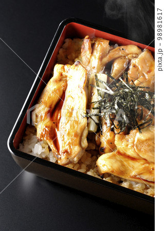 タレがたっぷりかかった熱々の炭火焼き鳥重を黒背景で俯瞰撮影 98981617