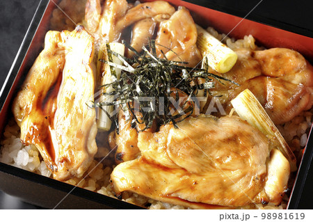 タレがたっぷりかかった熱々の炭火焼き鳥重を黒背景で俯瞰撮影 98981619