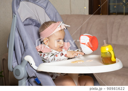 A cute one-year-old girl pours cookies out of a plate. Complementary foods for children, self-feeding, sugar in food. 98981622