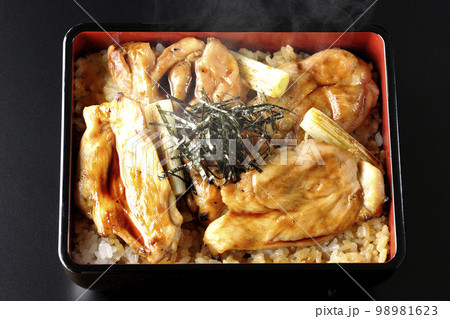 タレがたっぷりかかった熱々の炭火焼き鳥重を黒背景で俯瞰撮影 98981623