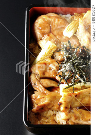 タレがたっぷりかかった熱々の炭火焼き鳥重を黒背景で俯瞰撮影 98981627