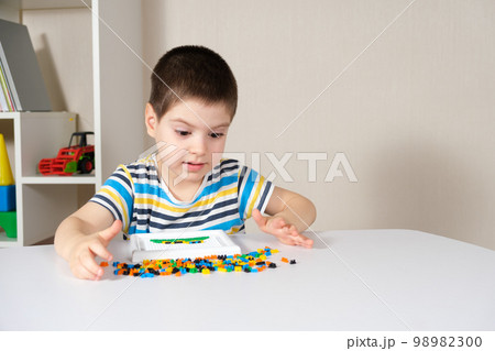 A boy of 4 years old plays with a mosaic, collects a picture from small plastic parts. Development of fine motor skills in children 98982300