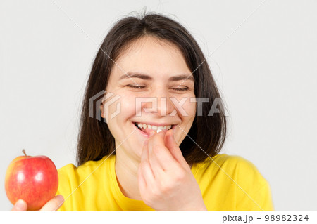 A happy healthy woman laughs and takes a vitamin pill or dietary supplement while holding an apple in her hand A happy healthy woman laughs and takes a vitamin pill or dietary supplement while holding an apple in her hand 98982324