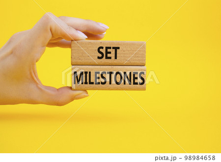 Set milestones symbol. Concept word Set milestones on wooden blocks. Beautiful yellow background. Businessman hand. Business and Set milestones concept. Copy space Set milestones symbol. Concept word Set milestones on wooden blocks. Beautiful yellow background. Businessman hand. Business and Set milestones concept. Copy space 98984658
