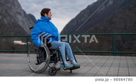 A woman in a wheelchair on a point view admires the high mountains. Thrust to life. A woman in a wheelchair on a point view admires the high mountains. Thrust to life. 98984780