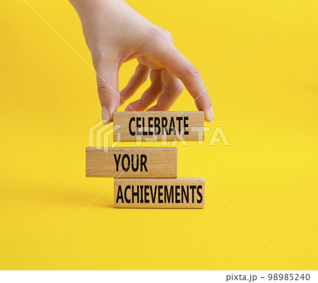 Celebrate your achievements symbol. Concept words Celebrate your achievements on wooden blocks. Beautiful yellow background. Businessman hand. Business concept. Copy space 98985240