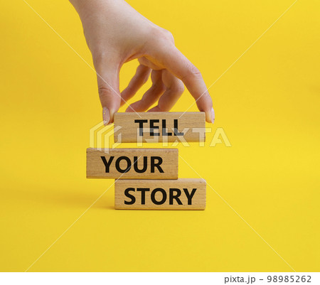 Tell your story symbol. Wooden blocks with words Tell your story. Beautiful yellow background. Businessman hand. Business and Tell your story concept. Copy space. 98985262
