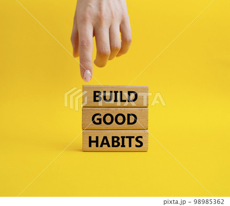 Build good habits symbol. Wooden blocks with words 'Build good habits'. Beautiful yellow background. Businessman hand. Business and 'Build good habits' concept. Copy space. 98985362
