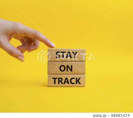 Stay on track symbol. Wooden blocks with words 'Stay on track'. Beautiful yellow background. Businessman hand. Business and 'Stay on track' concept. Copy space Stay on track symbol. Wooden blocks with words 'Stay on track'. Beautiful yellow background. Businessman hand. Business and 'Stay on track' concept. Copy space 98985424