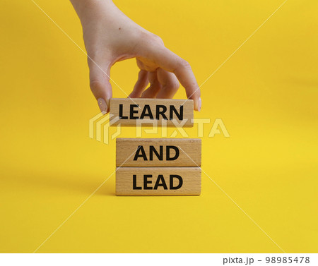 Learn and lead symbol. Concept words 'Learn and lead' on wooden blocks. Beautiful yellow background. Businessman hand. Business and Learn and lead concept. Copy space. 98985478
