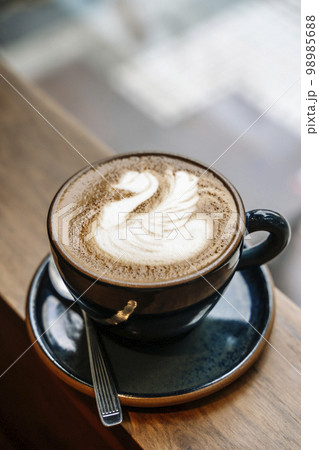 A cup of cappuccino coffee on a table in a cafe. Coffee hot drink in a ceramic cup for breakfast in the morning. 98985688