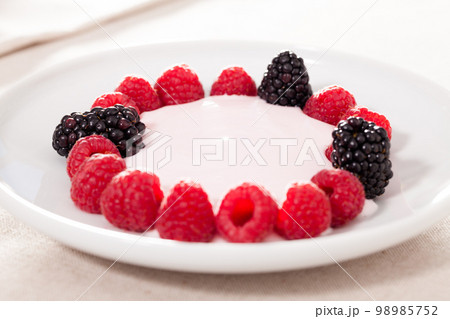 fresh raspberries and blackberries laid out on a white plate in circle with yogurt fresh raspberries and blackberries laid out on a white plate in circle with yogurt 98985752