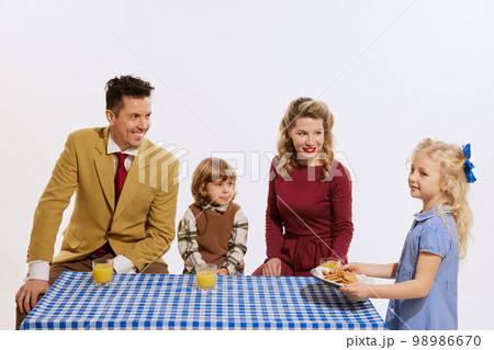 Friendly happy family, parents and kids standing around table isolated on white background. Concept of holidays, traditions, retro style, fashion, elegance, 60s, 70s, family. Friendly happy family, parents and kids standing around table isolated on white background. Concept of holidays, traditions, retro style, fashion, elegance, 60s, 70s, family. 98986670