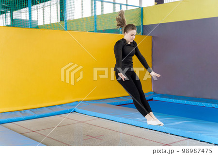 Teenage girl jumping on trampoline in fitness center Teenage girl jumping on trampoline in fitness center 98987475