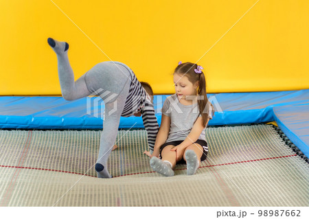 Happy smiling small kids sitting on indoor trampoline and playing in entertainment center Happy smiling small kids sitting on indoor trampoline and playing in entertainment center 98987662