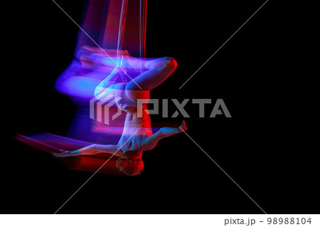 Balance. Young flexible girl doing aerial yoga, training over black studio background in neon with mixed lights. Concept of fitness and healthy lifestyle Balance. Young flexible girl doing aerial yoga, training over black studio background in neon with mixed lights. Concept of fitness and healthy lifestyle 98988104