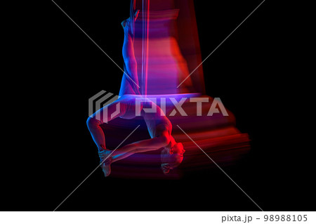 Stretching. Young flexible girl doing aerial yoga, training over black studio background in neon with mixed lights. Concept of fitness and healthy lifestyle Stretching. Young flexible girl doing aerial yoga, training over black studio background in neon with mixed lights. Concept of fitness and healthy lifestyle 98988105