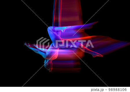 Young flexible girl doing aerial fly yoga, training over black studio background in neon with mixed lights. Concept of fitness and healthy lifestyle Young flexible girl doing aerial fly yoga, training over black studio background in neon with mixed lights. Concept of fitness and healthy lifestyle 98988106