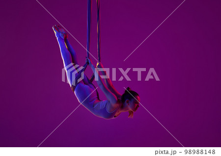 Strong body. Young flexible girl doing aerial yoga, training over purple studio background in neon light. Concept of fitness and healthy lifestyle 98988148