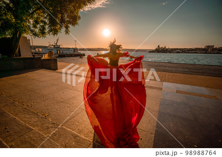 Sunrise red dress. A woman in a long red dress against the backdrop of sunrise, bright golden light of the sun's rays. The concept of femininity, harmony. 98988764