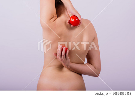 Healthy young woman holding tomatos over her eyes, laughing, bare shoulders, topless. 98989503