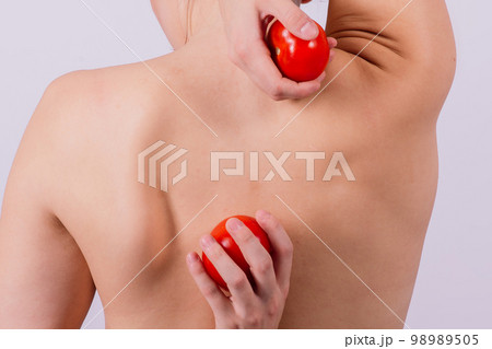 Healthy young woman holding tomatos over her eyes, laughing, bare shoulders, topless. 98989505