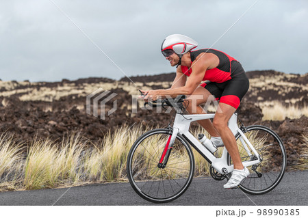 Cycling sport triathlete man biking on triathlon bike. Fit male cyclist on professional triathlon bicycle wearing aero helmet and trisuit for race in Kailua Kona, Big Island, Hawaii, USA 98990385