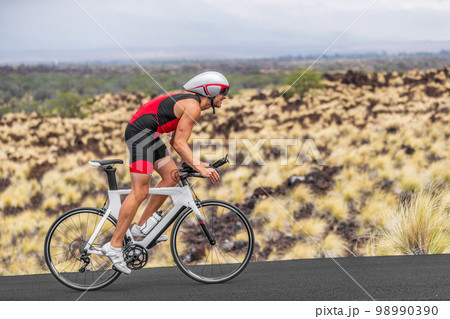 Cycling sport athlete man biking on triathlon bike. Fit male cyclist on professional triathlon bicycle wearing time trial helmet for iron man race exercising in Kailua Kona, Big Island, Hawaii, USA 98990390
