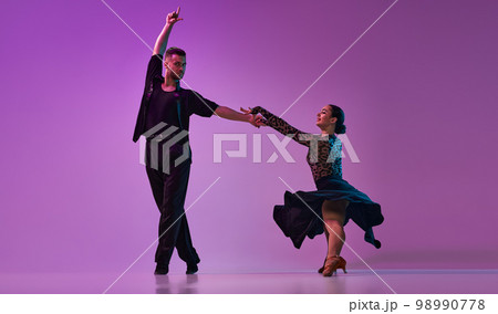 Talented young man and woman, professional dancers performing tango over purple background on neon lights. Concept of art, beauty, motion Talented young man and woman, professional dancers performing tango over purple background on neon lights. Concept of art, beauty, motion 98990778