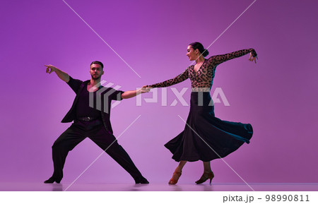 Talented young man and woman, professional dancers performing tango over purple background on neon lights. Concept of art, beauty, motion Talented young man and woman, professional dancers performing tango over purple background on neon lights. Concept of art, beauty, motion 98990811