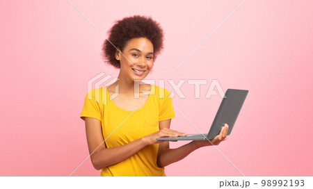 Glad smiling pretty young black curly lady working on laptop, enjoy study and work remotely Glad smiling pretty young black curly lady working on laptop, enjoy study and work remotely 98992193