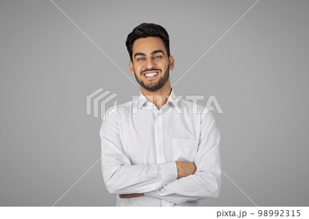 Smiling Handsome Young Arab Businessman With Folded Arms Standing Over Grey Background 98992315