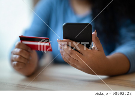 Unrecognizable dark-skinned woman holding phone and bank card Unrecognizable dark-skinned woman holding phone and bank card 98992328