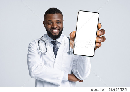 Medical Offer. Black Male Doctor In Uniform Demonstrating Smartphone With Blank Screen 98992526