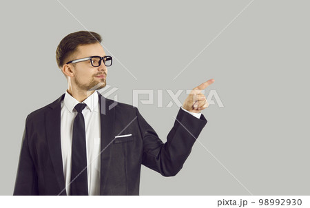 Confident handsome young businessman pointing finger at content or copy space on gray background. 98992930