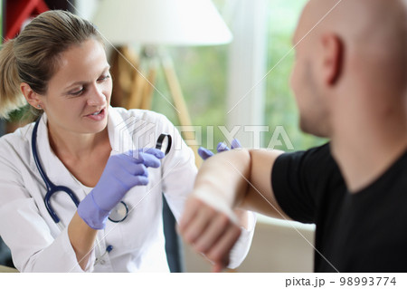 Gloved woman dermatologist examining skin of bald patient with magnifying glass. 98993774