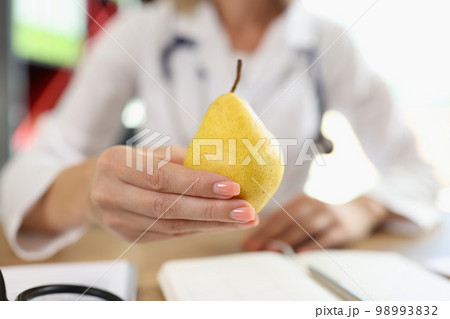 Close-up of pear in hand of nutritionist above medical office table. Close-up of pear in hand of nutritionist above medical office table. 98993832