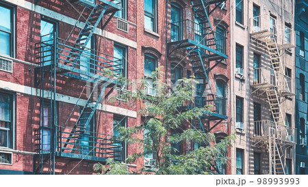 Old brick townhouses with fire escapes, color toning applied, New York City, USA. 98993993